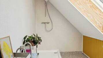A small, modern bathroom with a shower, a sink, and a potted plant.