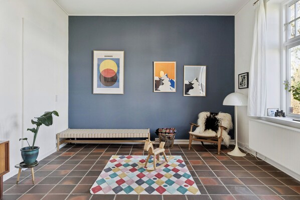 Una habitación con pared azul, un banco, una mecedora, un tapete colorido y obras de arte enmarcadas.