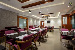 A modern dining area with multiple tables and chairs, a stone wall, and a wooden ceiling.