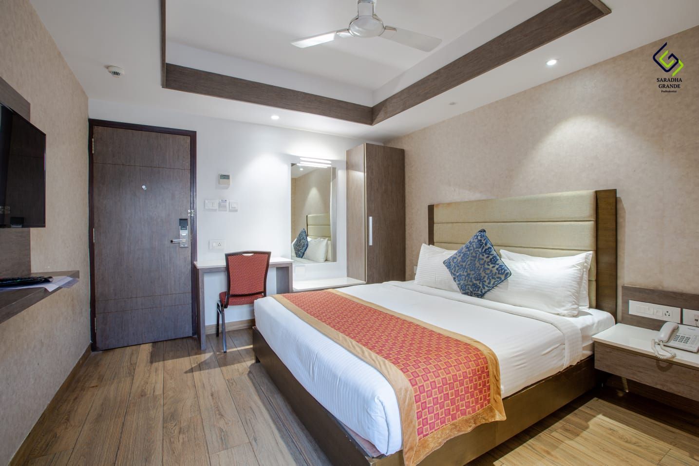 A hotel room with a bed, a desk, a chair, a wardrobe, and a mirror.