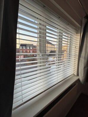 A window with horizontal blinds, a view of buildings outside, and a vent below the window. - A&R Guest House - 2-bed Coach House, Bristol (Bristol)