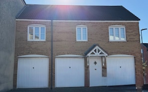 A two-story residential building with a brick facade, three garage doors, and a small triangular window above the central garage door. - A&R Guest House - 2-bed Coach House, Bristol (Bristol)