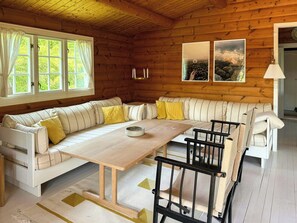 Ein gemütliches Blockhaus-Interieur mit Holzausstattung, einer Couch, einem Esstisch und zwei gerahmten Bildern an der Wand.