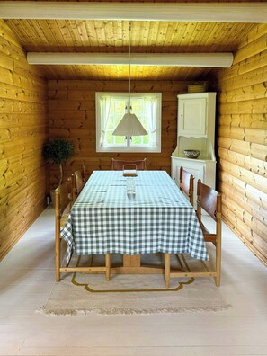 Interior d'una cabana de fusta amb taula de dinar preparada per a quatre, una finestra amb cortines i un armari.