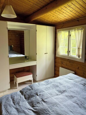 Un dormitori amb un llit, un armari, un mirall, una finestra amb cortines i una làmpada penjant.