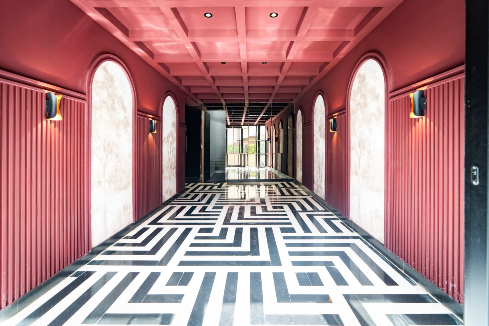 A corridor with a geometric patterned floor, arched doorways, and wall-mounted light fixtures.
