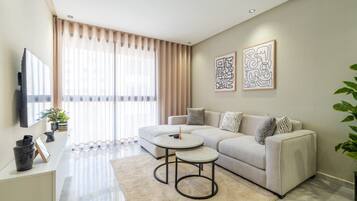 A modern living room with a sofa, two side tables, a flat-screen TV, and artwork on the wall.