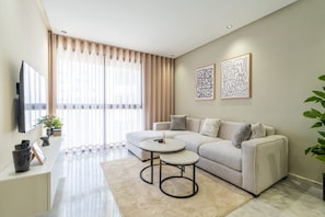 A modern living room with a sofa, two side tables, a flat-screen TV, and artwork on the wall.