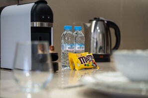 Una encimera de cocina con una cafetera, dos botellas de agua, un hervidor y un paquete de M&Ms.