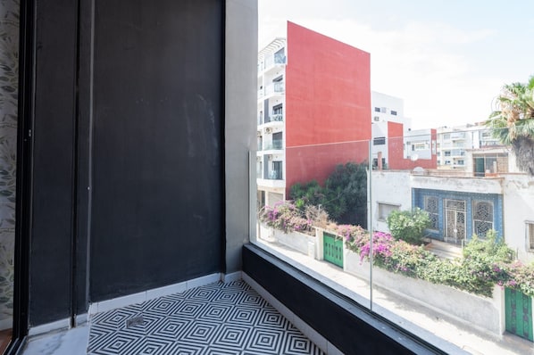 A room with a large window, black and white patterned floor, and a view of buildings with balconies.