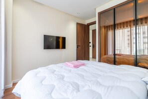 A hotel room with a large bed, a flat-screen TV mounted on the wall, and a sliding door leading to a balcony.