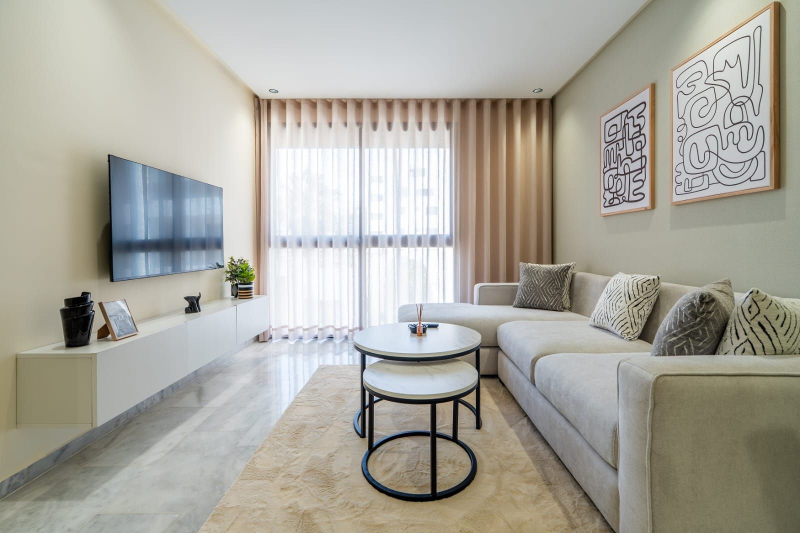 A modern living room with a flat-screen TV, a round coffee table, a sofa, and a large window with curtains.