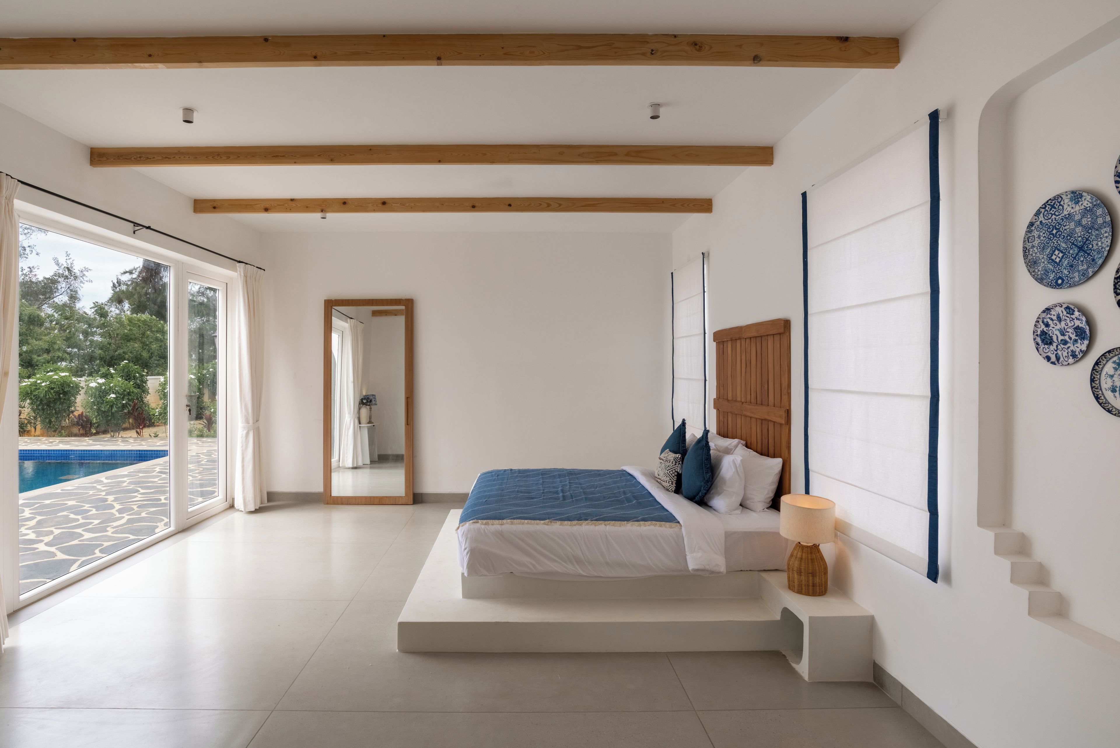 Un dormitorio con una cama grande, techo de madera, vista a una piscina y un espejo.