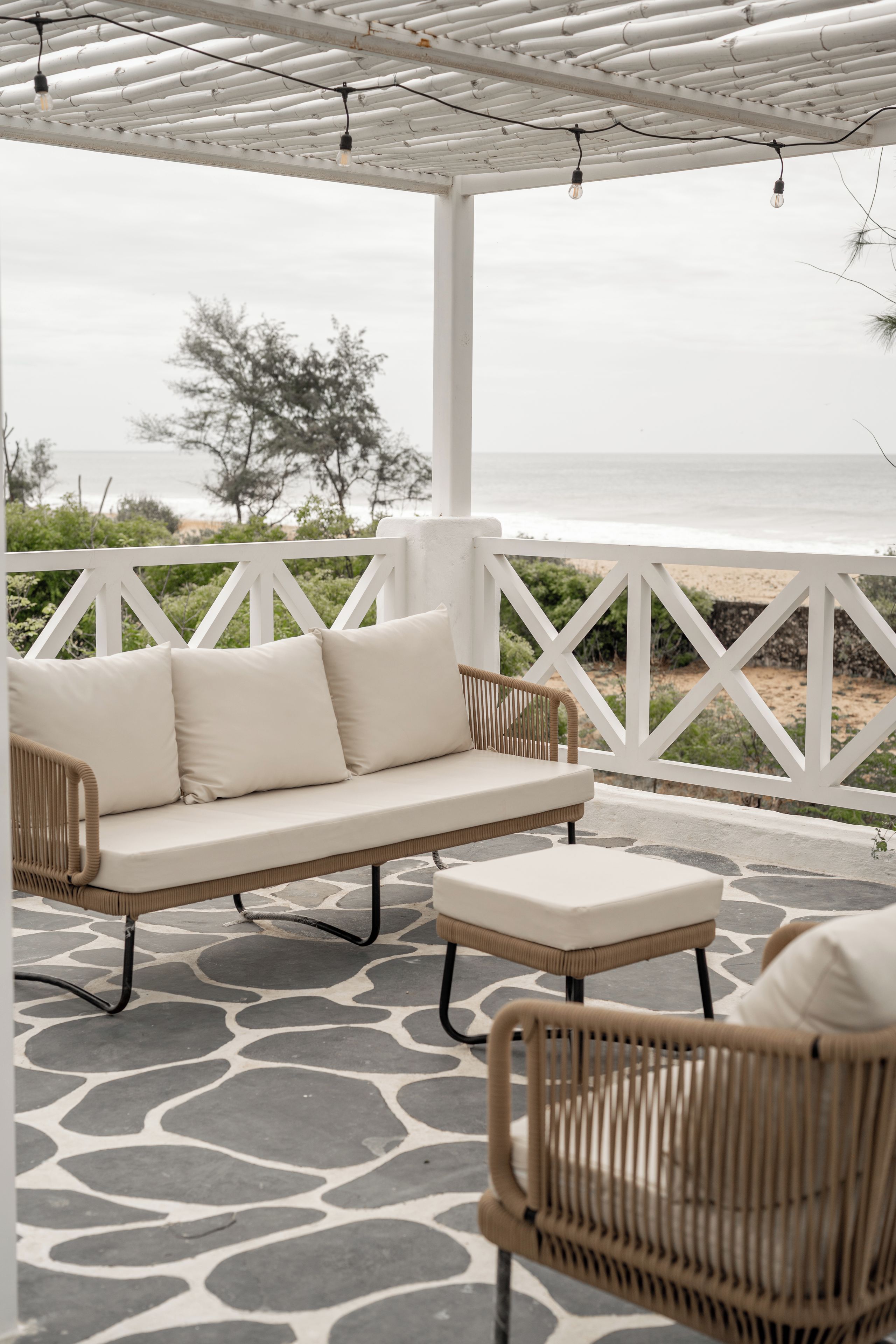 A covered outdoor seating area with a sofa and chairs, a patterned floor, and a view of the sea.