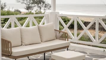 A covered outdoor seating area with a sofa and chairs, a patterned floor, and a view of the sea.