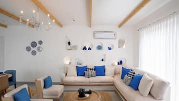 Una sala de estar moderna con un sofá color beige, cojines azules, una mesa de centro de madera y una lámpara de araña.