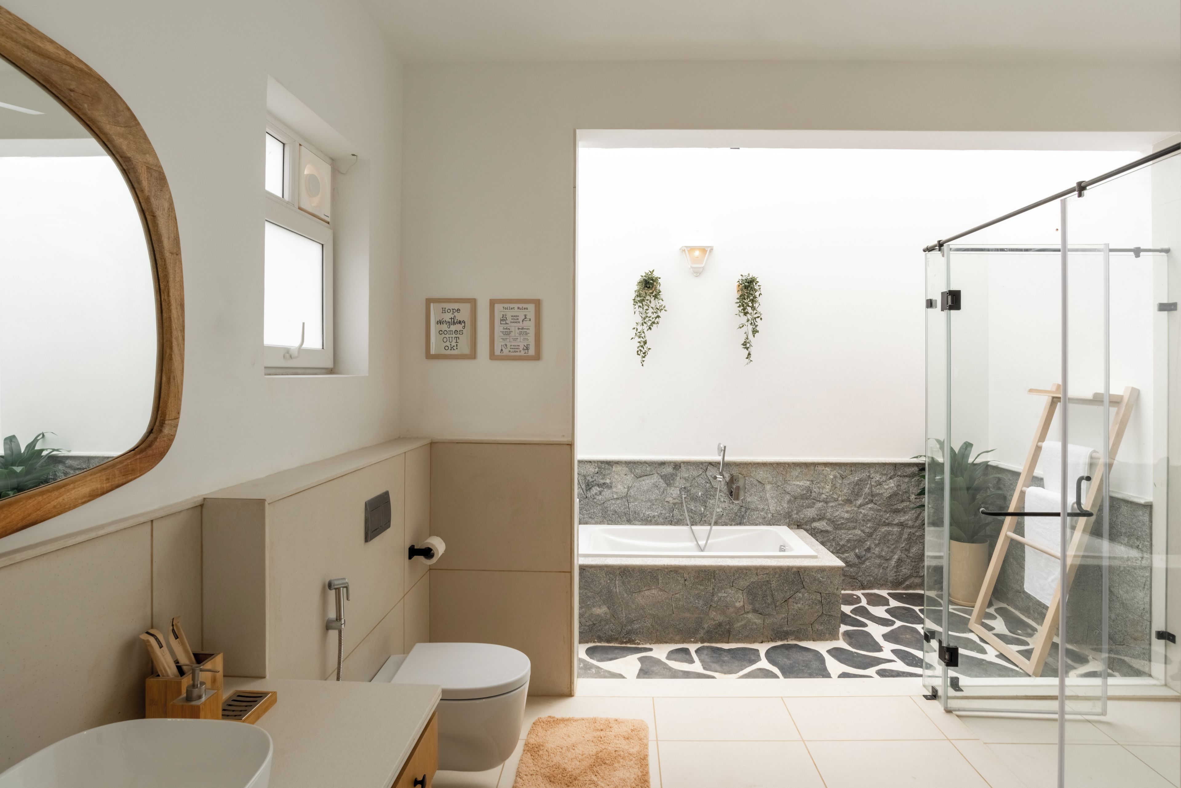 A modern bathroom with a bathtub, shower, toilet, and sink. There are two framed pictures on the wall and a mirror.