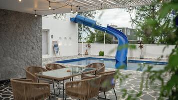 Ein Außenpoolbereich mit einer blauen Rutsche, Korbmöbeln und Lichterketten.