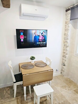 A room with a flat-screen TV mounted on the wall, a wooden table with two woven placemats, white chairs, and a small potted plant. - 16097522 FRGK 5-Apartment Building - Downtown Cannes - Conference Special - 47 rue Meynadier (Cannes)