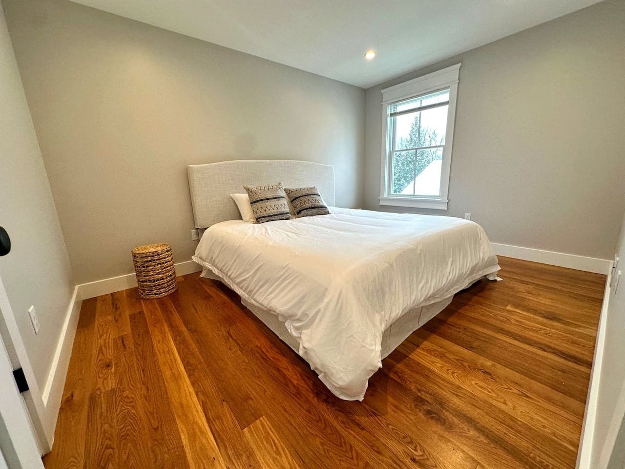 Een slaapkamer met een bed, een raam en een houten vloer.