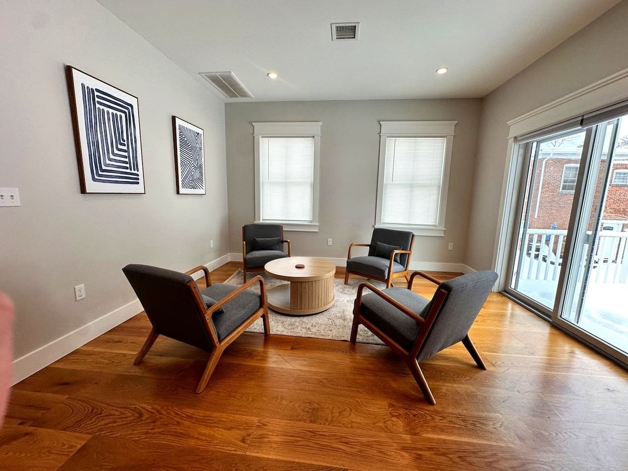 A spacious living room with hardwood flooring, a central coffee table, and four armchairs arranged around it.