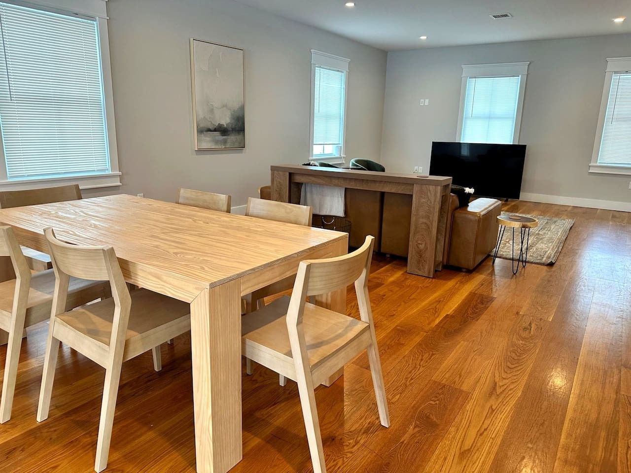 A modern living room with a wooden dining table and chairs, a TV, and a kitchen area.