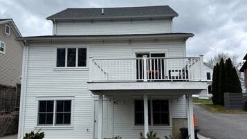 A two-story residential building with a balcony, a front porch, and a driveway.