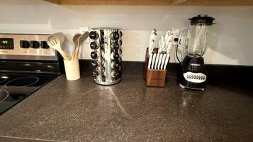 Un plan de travail de cuisine avec une cuisinière, une machine à café, un mixeur et des supports pour ustensiles.