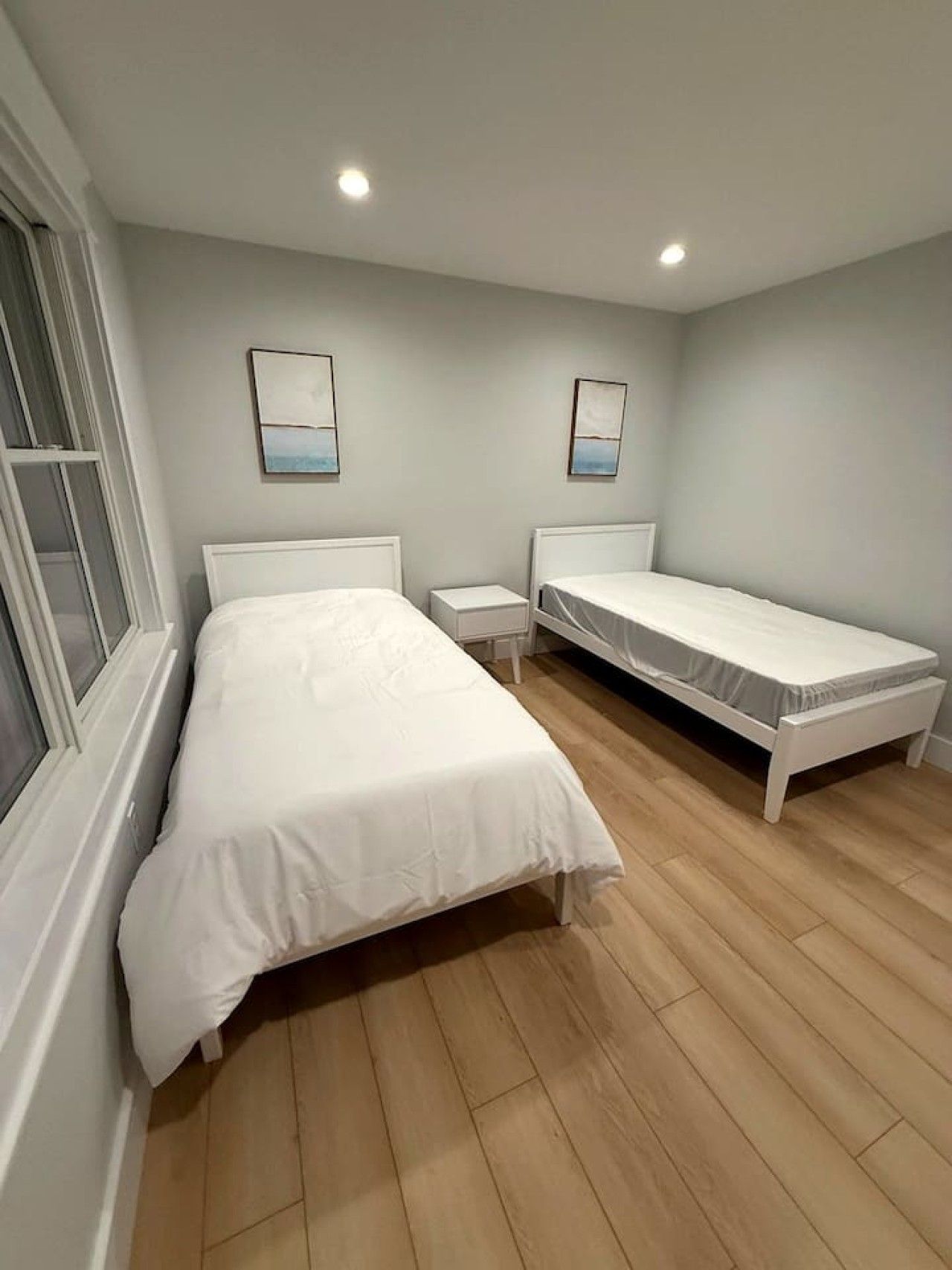 Ein Schlafzimmer mit einem großen Bett, einem kleineren Bett, einem Nachttisch und einem Fenster.