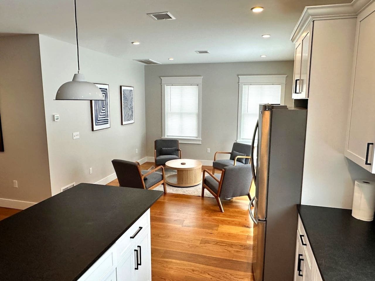 A modern kitchen with a dining area, wooden flooring, and a refrigerator.