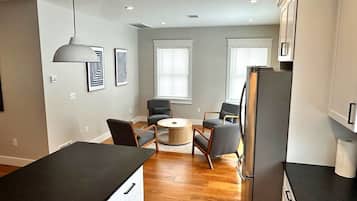 A modern kitchen with a dining area, wooden flooring, and a refrigerator.