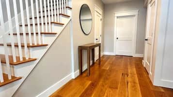 A hallway with wooden flooring, white walls, a staircase with white railings, and a door at the end.