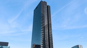 A tall, modern skyscraper with a reflective glass facade. - Home Views on Collins – light filled CBD apartment with pool, gym and elevated views (Melbourne)