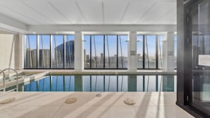 Una piscina interior moderna con vistas despejadas a un paisaje urbano a través de amplios ventanales.