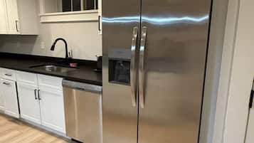 A modern kitchen with stainless steel appliances, white cabinetry, and a wooden floor.