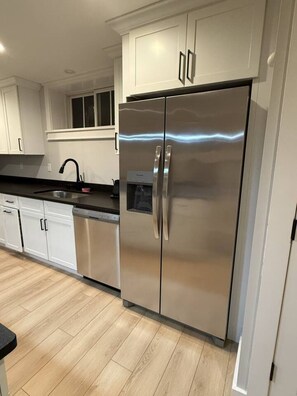A modern kitchen with stainless steel appliances, white cabinetry, and a wooden floor.