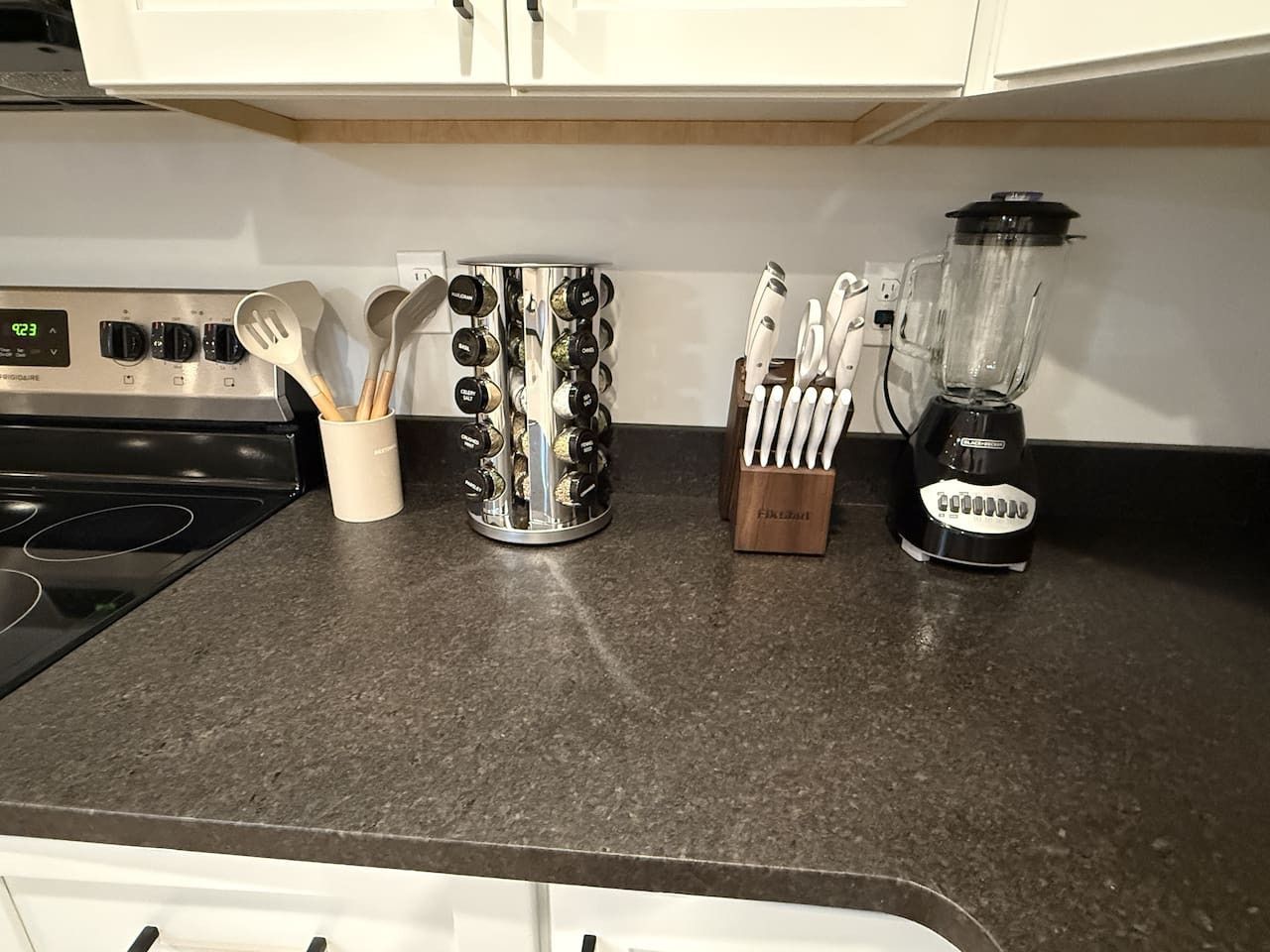 A kitchen counter with a stove, a set of utensils, a spice rack, and a blender.
