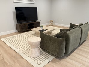 Una sala de estar moderna con un televisor de pantalla plana, un sofá gris, una mesa de centro y un tapete estampado.
