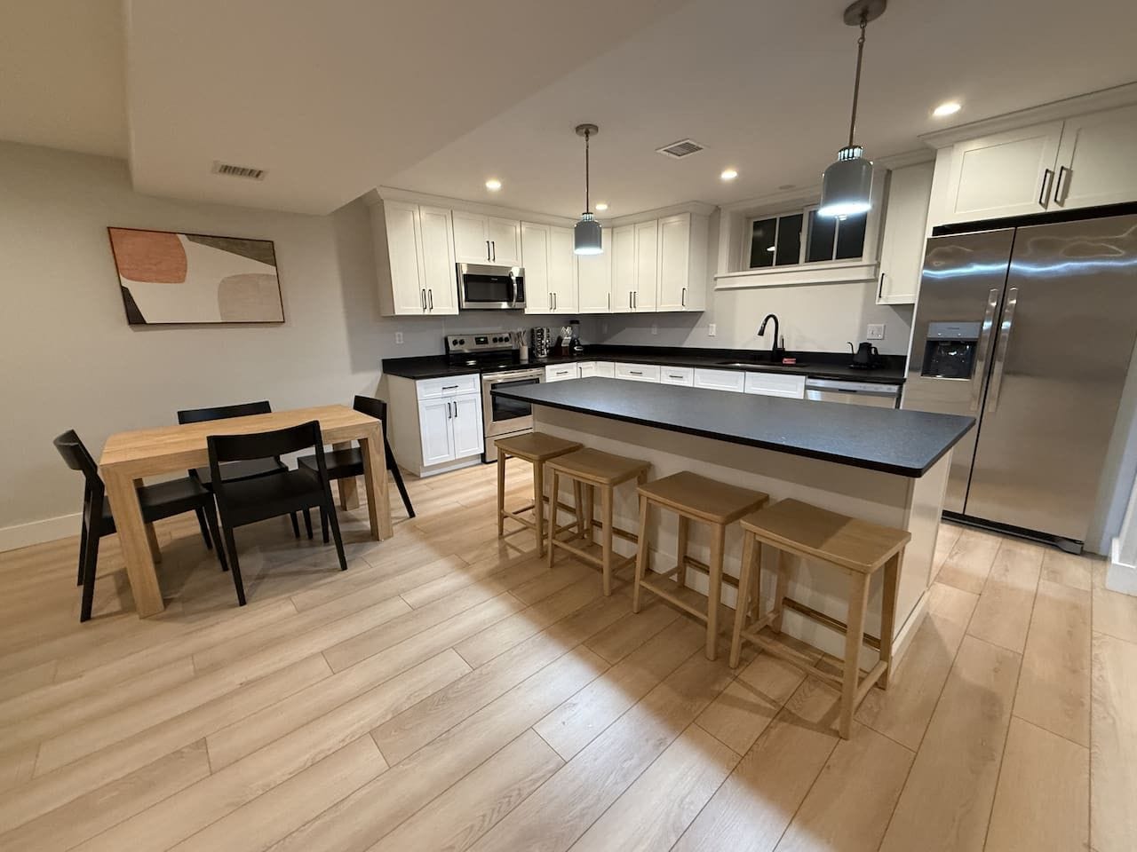 Een moderne keuken met een centraal eiland, houten barstoelen en een eettafel met stoelen.