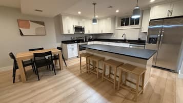 Een moderne keuken met een centraal eiland, houten barstoelen en een eettafel met stoelen.