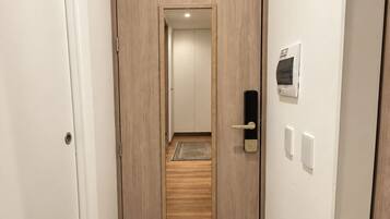 Un pasillo con una puerta de madera, un felpudo y un interruptor de luz en la pared.