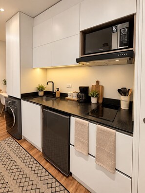 Cozinha moderna com armários brancos, bancada preta, micro-ondas embutido e máquina de lavar louça.