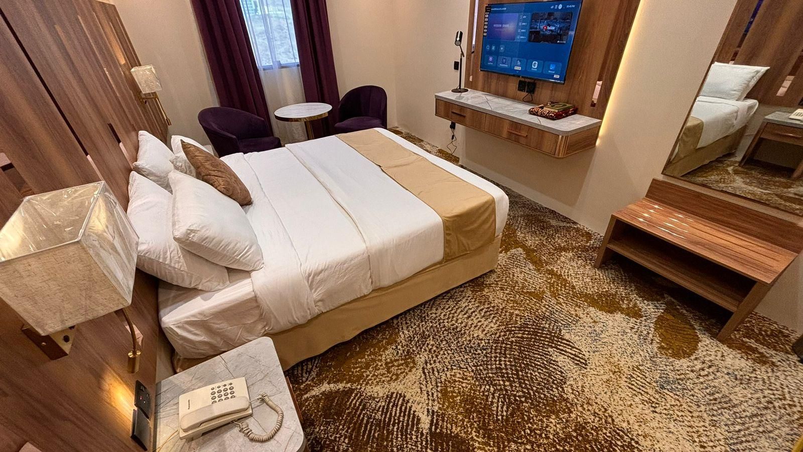Una habitación de hotel con cama, escritorio con teléfono, televisor y una mesita.