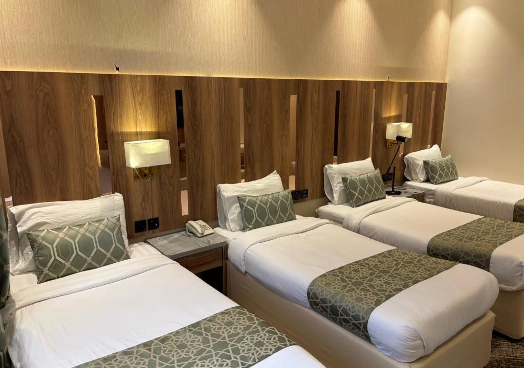 Una habitación de hotel con cuatro camas, cada una con almohada y manta. Hay lámparas de noche y un teléfono en la mesita.
