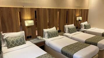 Una habitación de hotel con cuatro camas, cada una con almohada y manta. Hay lámparas de noche y un teléfono en la mesita.
