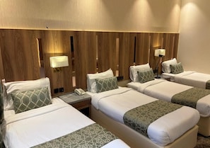 Una habitación de hotel con cuatro camas, cada una con almohada y manta. Hay lámparas de noche y un teléfono en la mesita.