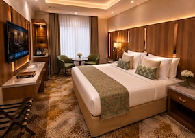 Habitación de hotel con una cama grande, un escritorio con televisión de pantalla plana, una pequeña mesa con sillas y vistas al exterior a través de la ventana.