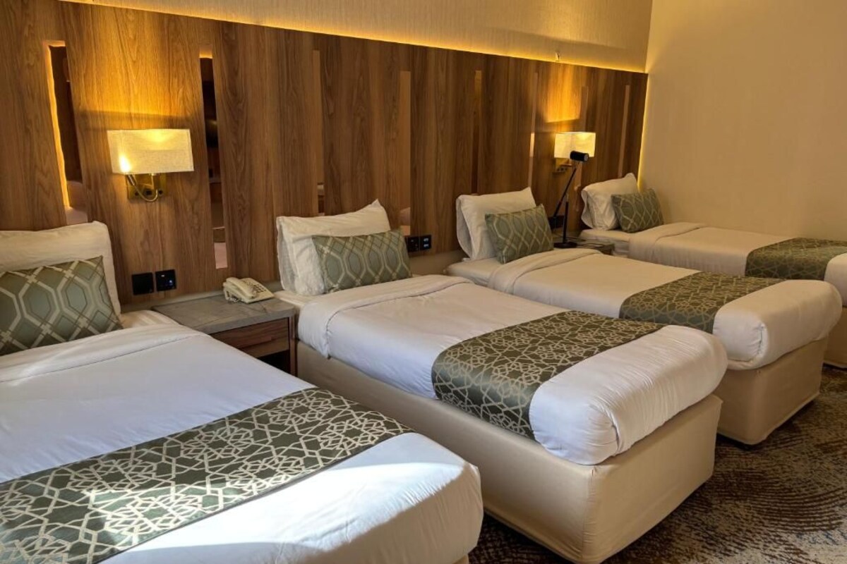A hotel room with four beds arranged in a row, each with a pillow and a bedside table.