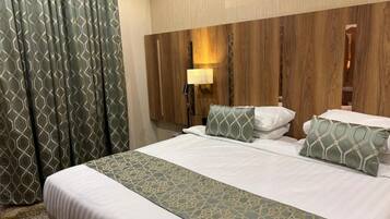 A hotel room with a large bed, a headboard with a light fixture, and a patterned curtain.