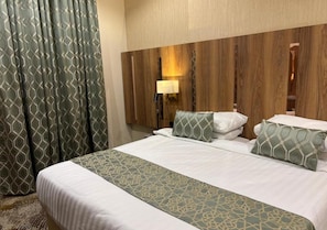 A hotel room with a large bed, a headboard with a light fixture, and a patterned curtain. - HINDIBAA HOTEL MAKKAH (Makkah)